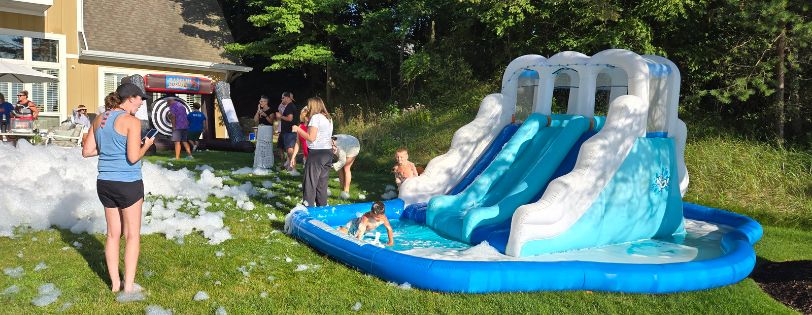 Kids enjoying a foam-covered inflatable water slide at an outdoor event hosted by Sammy's Party On Wheels.