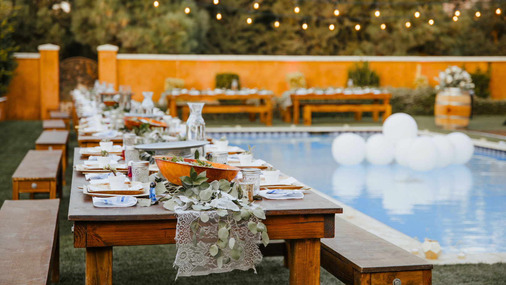 Planning a Backyard Wedding? Here’s How to Create the Perfect Vibe 1 backyard wedding dj. Elegant backyard wedding reception setup with wooden tables by a pool, decorated with greenery and lace runners